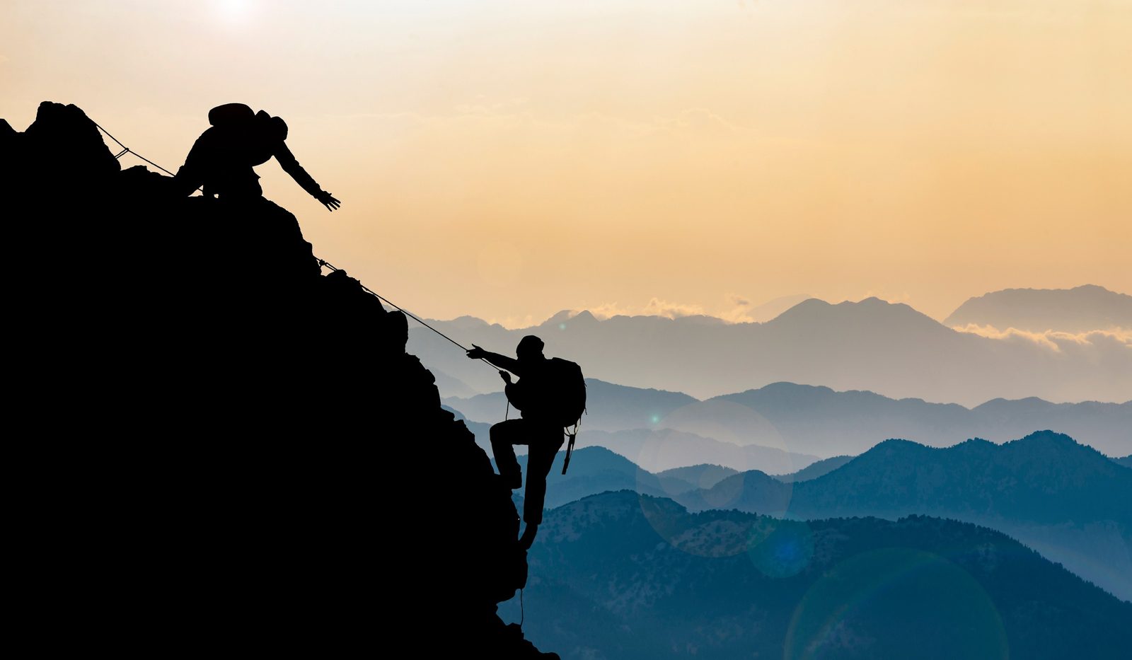 Two climbers on a mountain — one reaching down to help the other up